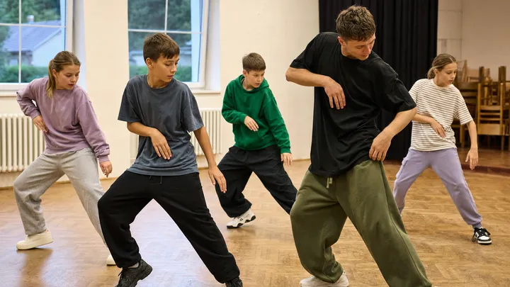 Děti nacvičují streetdanceovou sestavu v českém komunitním sále s lektorkou; ilustrační fotografie s fiktivními osobami.